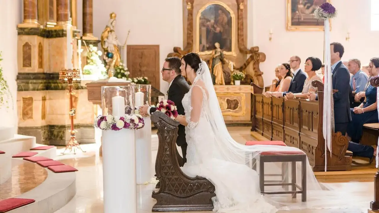 Brautpaar kniet vor dem Altar. Sie heiraten kirchlich, nur ein Partner in der Kirche. Gäste sitzen auf den Bänken.