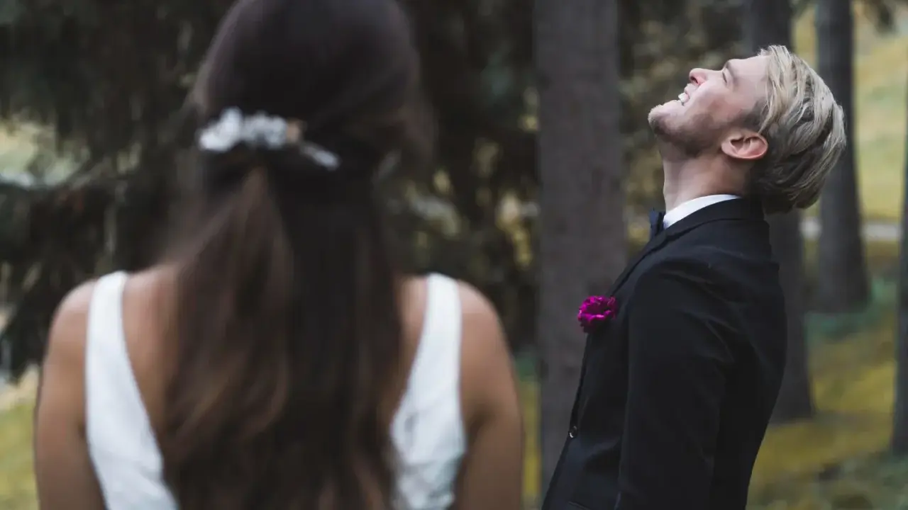 Ein Bräutigam lacht mit geschlossenen Augen in den Himmel, während die Braut ihm den Rücken zukehrt. Vielleicht ist es die Angst vor der Hochzeit, die ihn so überwältigt.