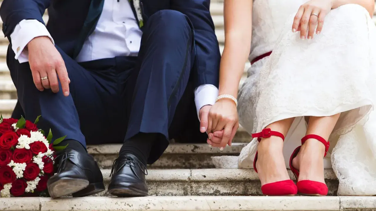 Brautpaar hält Händchen, rote Rosen und rote Schuhe. Die Frage "wie kurzfristig kann man heiraten" beschäftigt viele Paare.
