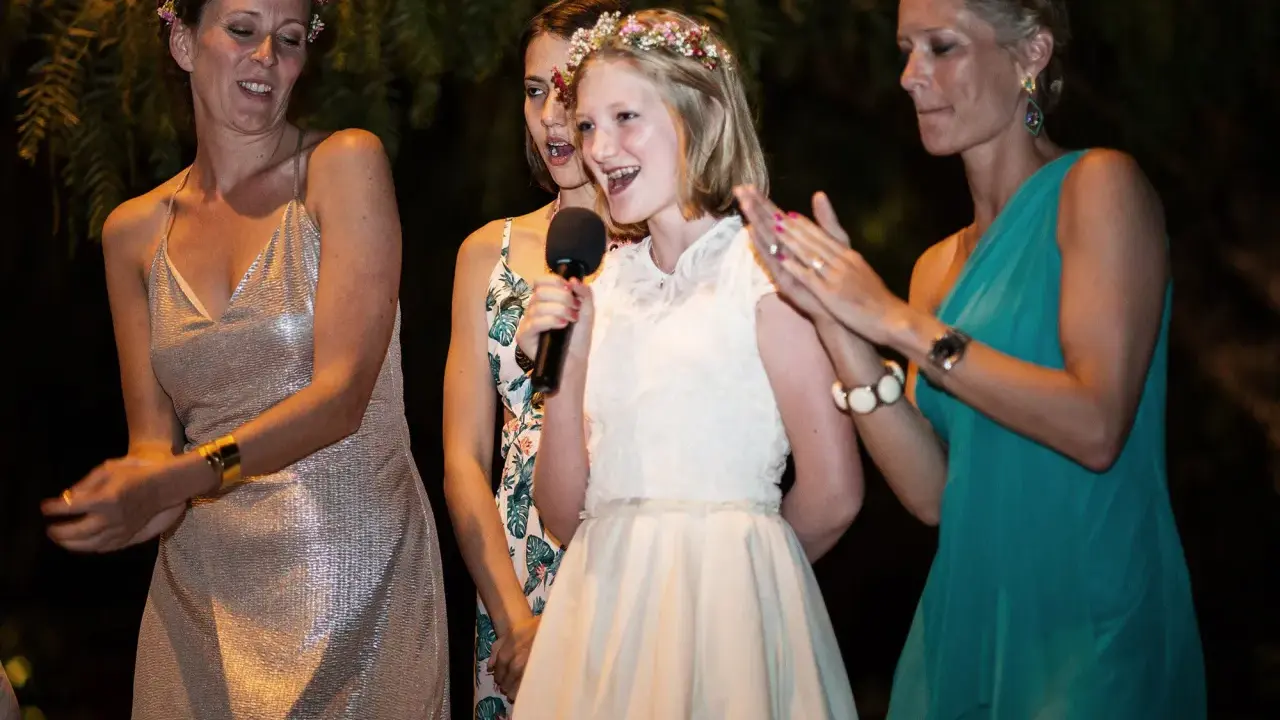Mädchen hält Mikrofon, während ihre Schwester und andere Frauen bei einer Hochzeitsrede applaudieren.