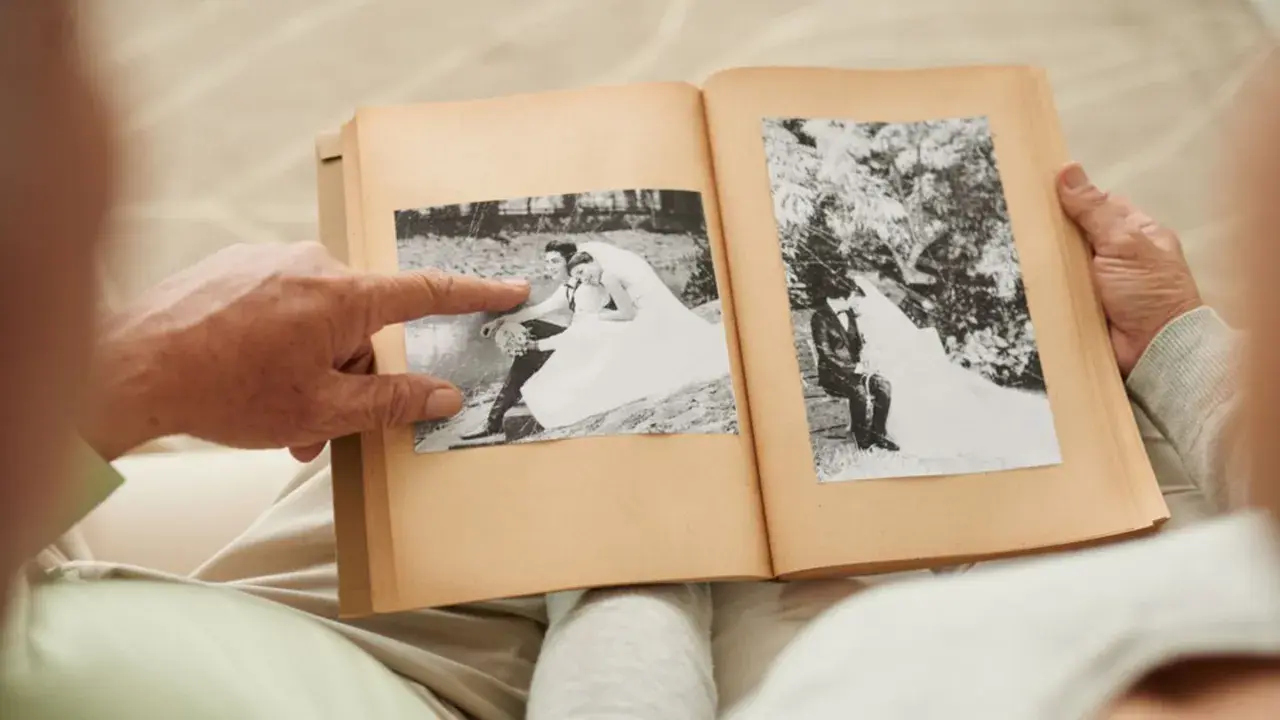 Ein älteres Paar blättert in einem Fotoalbum. Ein Finger zeigt auf ein Hochzeitsfoto. Wie viele Jahre ist die Gnadenhochzeit her?