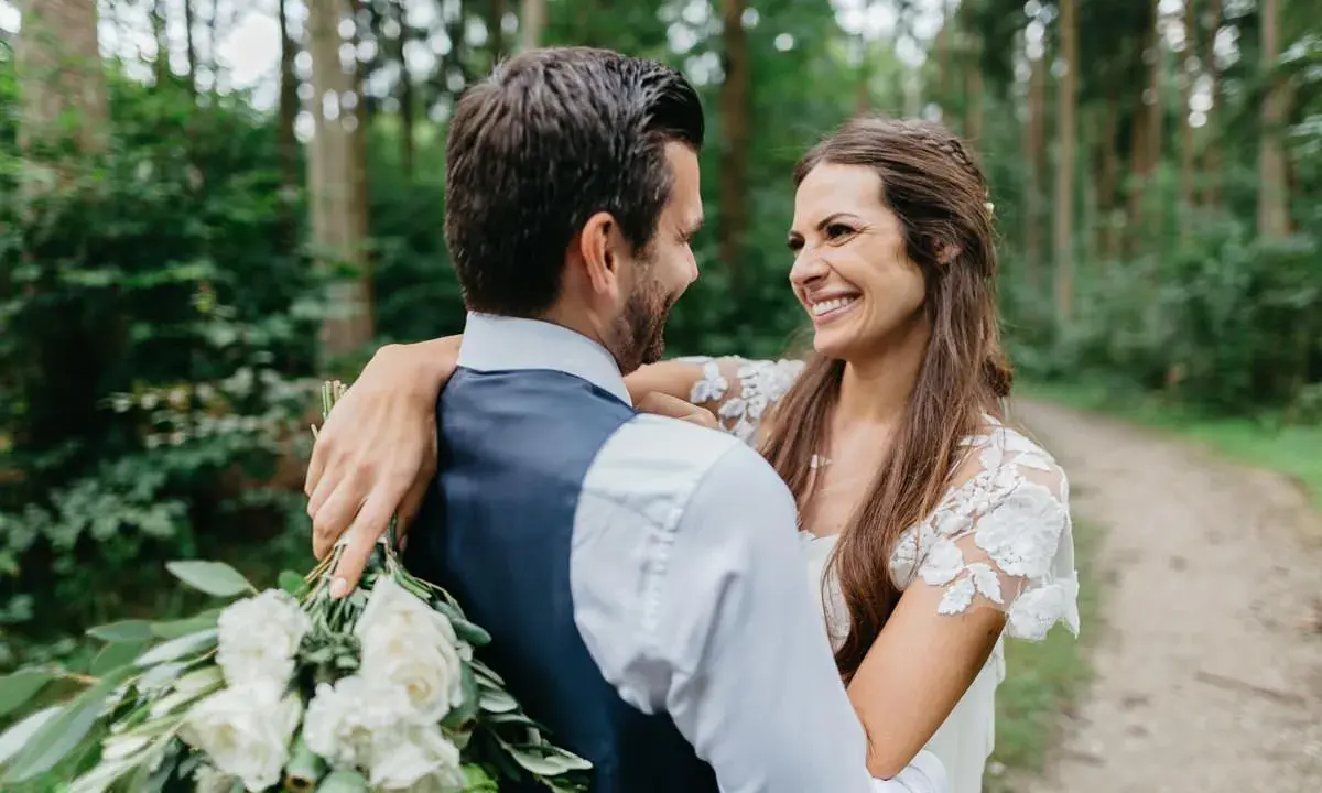 Ein glückliches Brautpaar umarmt sich im Wald. Sie wollten heimlich heiraten und genießen diesen intimen Moment.