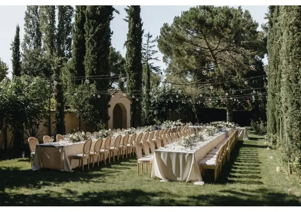 Festlich gedeckte lange Tafel im Garten, umgeben von Zypressen und Bäumen. Perfekt für Hochzeitslocation-Fragen.