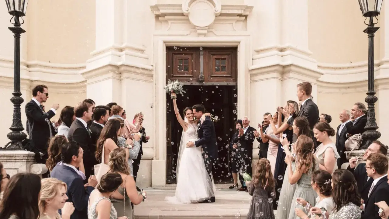 Ein strahlendes Brautpaar verlässt die Kirche, umgeben von Seifenblasen und jubelnden Gästen. Eine klassische Hochzeit voller Freude und Romantik.
