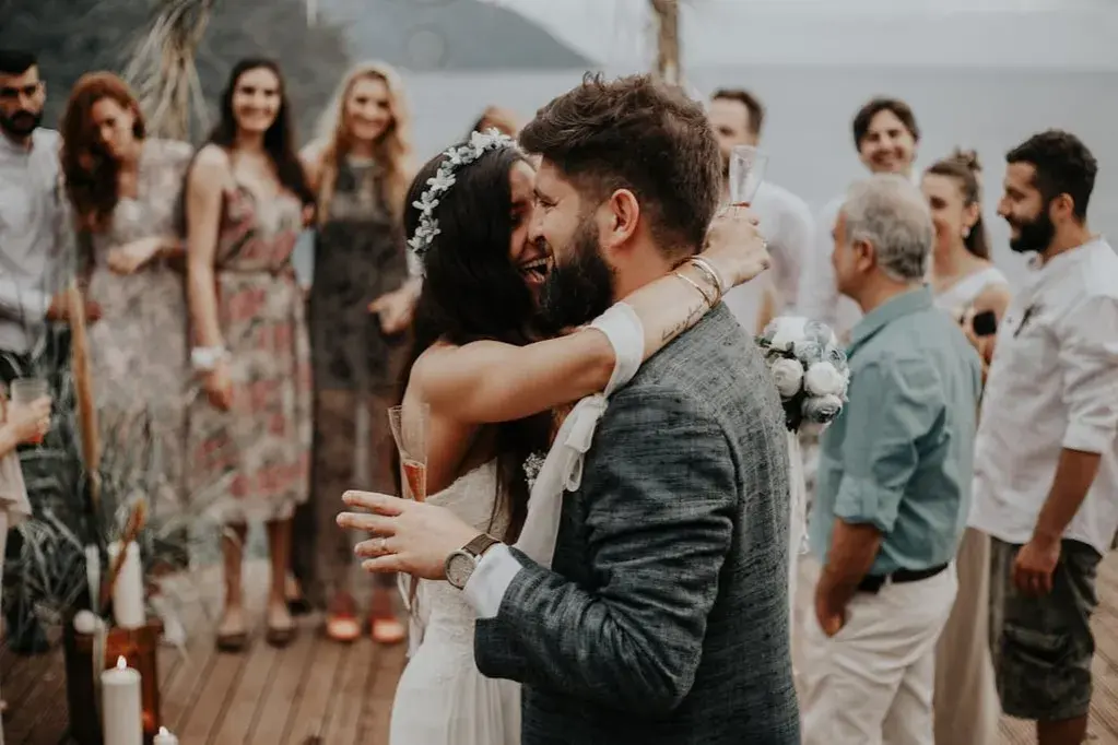 Glückliches Brautpaar umarmt sich, Gäste im Hintergrund. Perfekt für zitate hochzeitskarte.