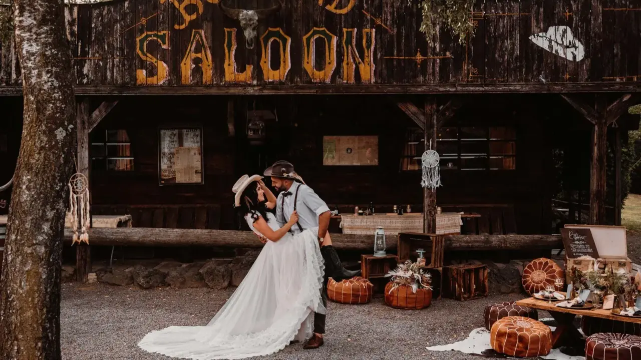 Ein Brautpaar feiert seine western hochzeit vor einem Saloon. Sie tanzen ausgelassen, umgeben von rustikaler Deko.