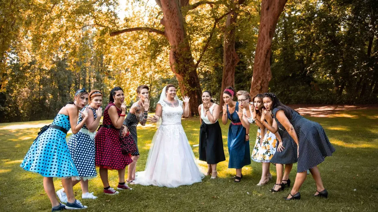 Brautjungfern in Polka-Dot-Kleidern und die Braut in Weiß posieren für eine fröhliche Rockabilly-Hochzeit im Freien.