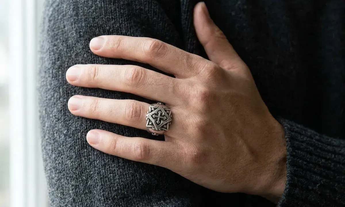 Ein Mann trägt einen detailreichen Ring mit Kreuzmuster an der linken Hand.