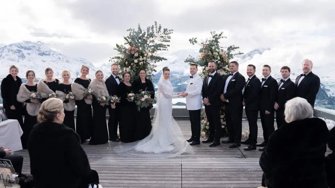 Brautpaar und Hochzeitsgesellschaft vor schneebedeckten Bergen. Eine wunderschöne Hochzeit in den Bergen mit Brautjungfern in schwarzen Kleidern und Männern in Anzügen.