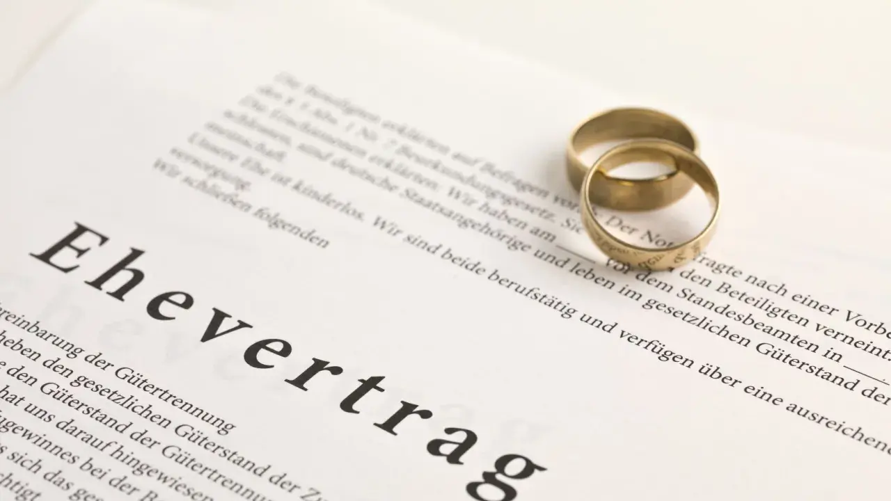 Zwei goldene Eheringe liegen auf einem Dokument mit der Überschrift "Ehevertrag". Eine Ehevertrag Vorlage, die die rechtlichen Vereinbarungen für die Ehe festhält.