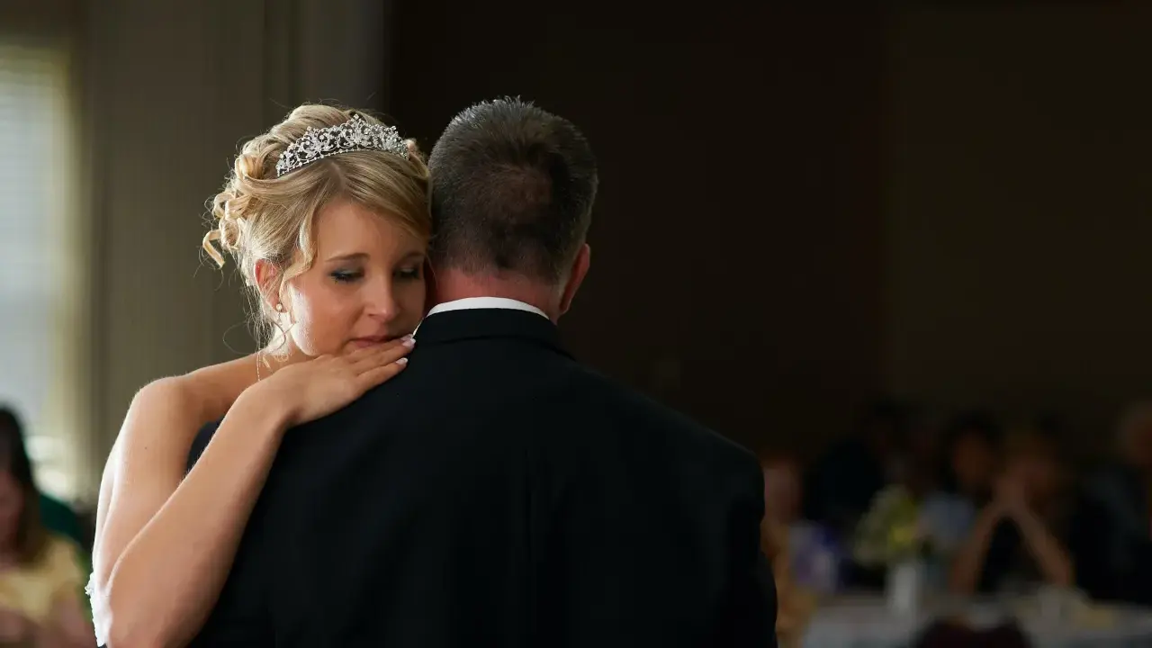 Ein zärtlicher Vater-Tochter-Tanz. Die Braut mit Diadem lehnt sich an ihren Vater, der einen schwarzen Anzug trägt.