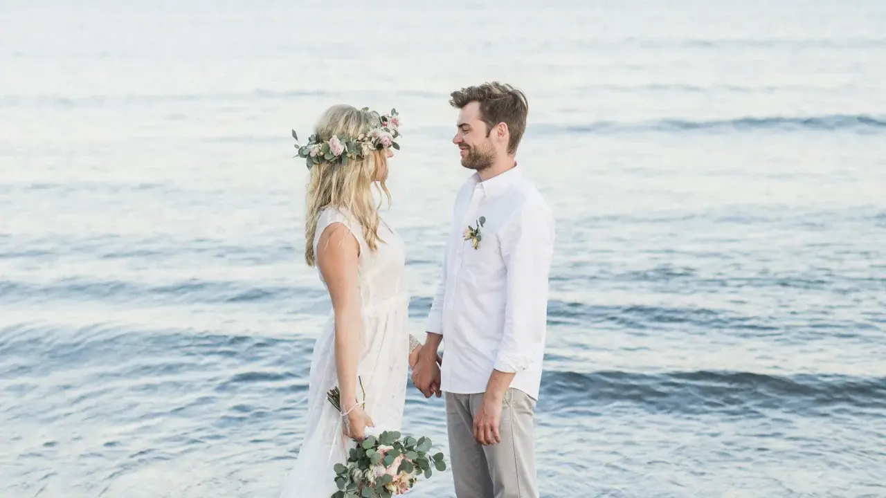 Ein glückliches Paar feiert seine Hochzeit am Strand zu zweit. Die Braut trägt einen Blumenkranz, der Bräutigam ein weißes Hemd.
