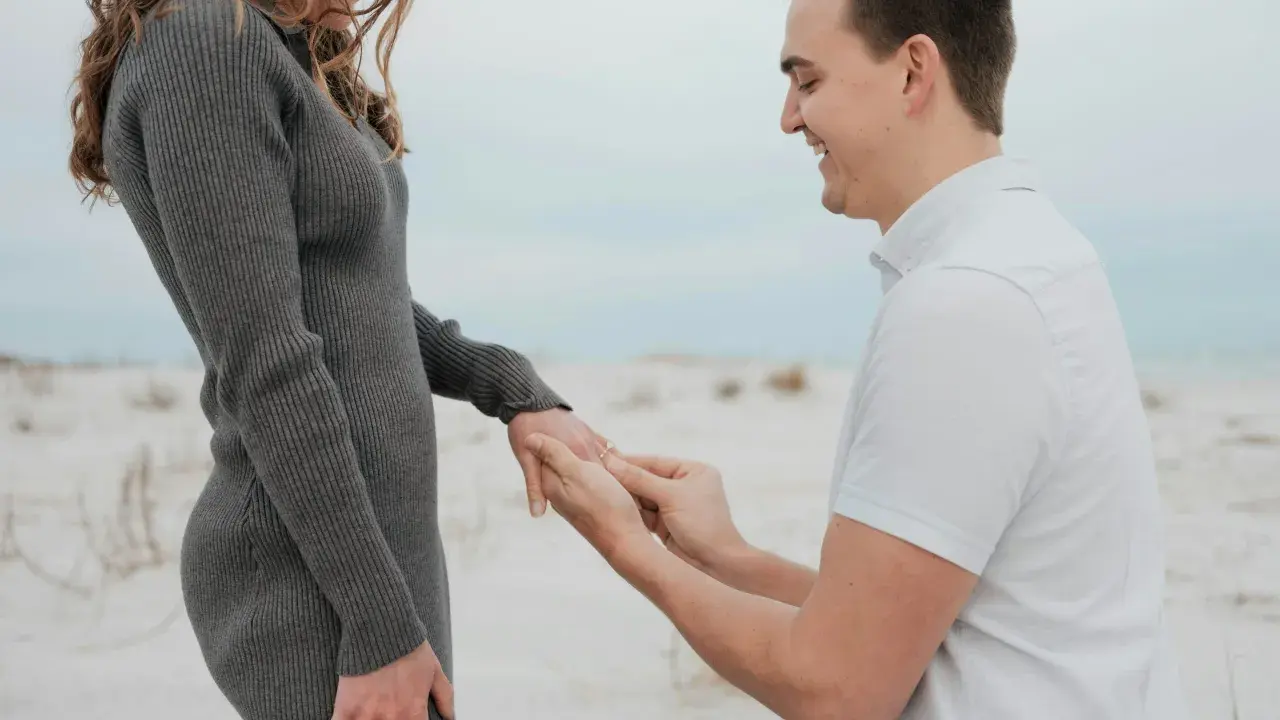 Ein Mann kniet am Strand und steckt seiner lachenden Partnerin einen Ring an den Finger. Ein Moment, der die tiefe **Verlobung Bedeutung** symbolisiert.