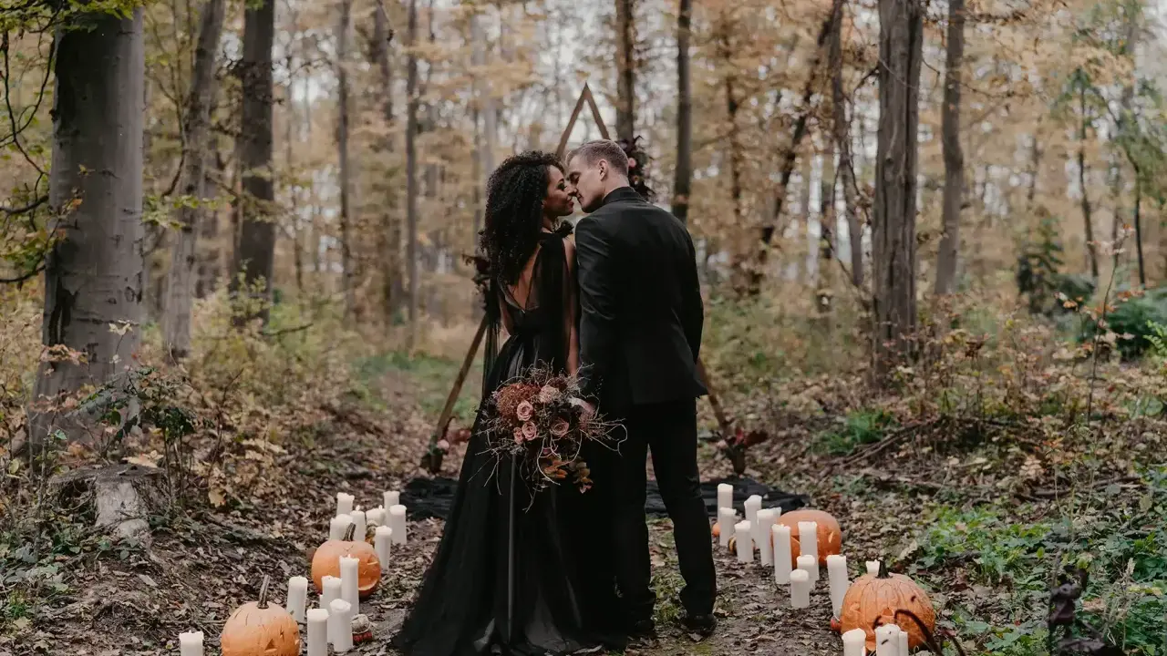 Ein Brautpaar küsst sich im Wald bei Kerzenlicht und Kürbissen. Eine romantische Halloween-Hochzeit im Herbst.
