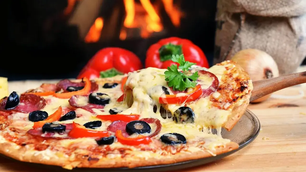Eine dampfende Pizza mit Salami, Oliven und Paprika, perfekt für den Mitternachtssnack zur Hochzeit, vor einem knisternden Kaminfeuer.