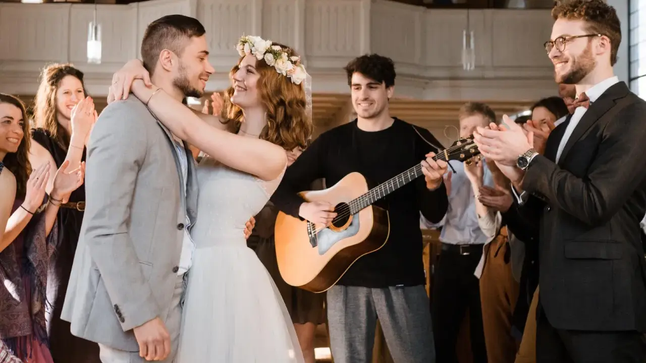 Glückliches Brautpaar umarmt sich, während ein Gitarrist spielt und Gäste applaudieren. Die Stimmung ist festlich, wie bei schönen Hochzeitsliedern auf Deutsch.