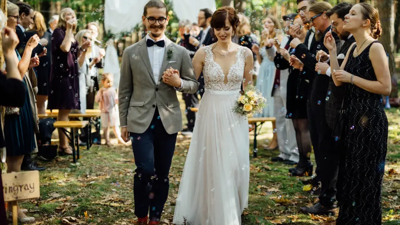 Brautpaar schreitet durch Seifenblasen, Gäste feiern Hochzeit locker.