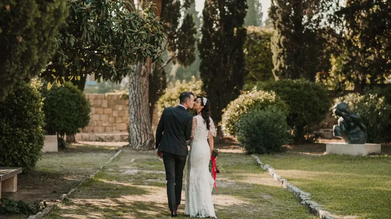 Ein Brautpaar küsst sich im Park. Die Braut trägt ein Spitzenkleid, der Bräutigam einen dunklen Anzug. Eine kroatische Hochzeit im Grünen.