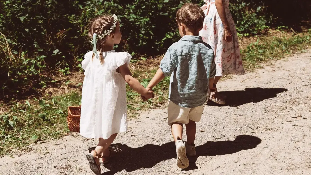 Zwei Kinder, ein Mädchen mit Blumenkranz und ein Junge, halten Händchen auf dem Weg zu einer Hochzeit mit Kindern.