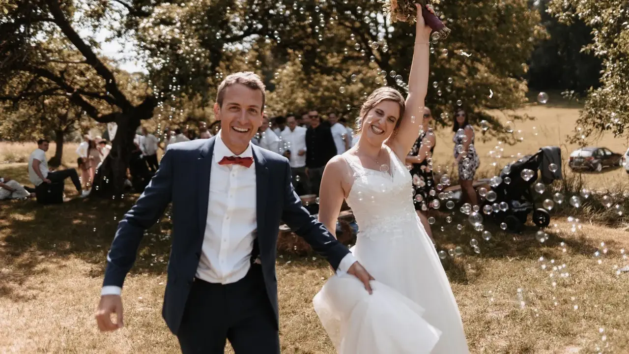 Glückliches Brautpaar im Freien, umgeben von Seifenblasen. Sie strahlen und scheinen gerade ihren Hochzeitstanz gelernt zu haben und feiern diesen besonderen Moment.