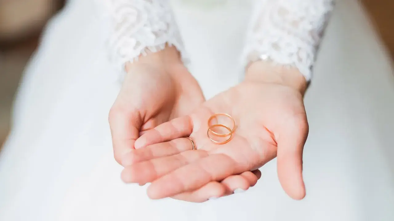 Zwei goldene Eheringe liegen in den Händen einer Braut. Sie sind ein Symbol für ihre bevorstehenden Hochzeitstage und die Namen, die sie für immer verbinden werden.
