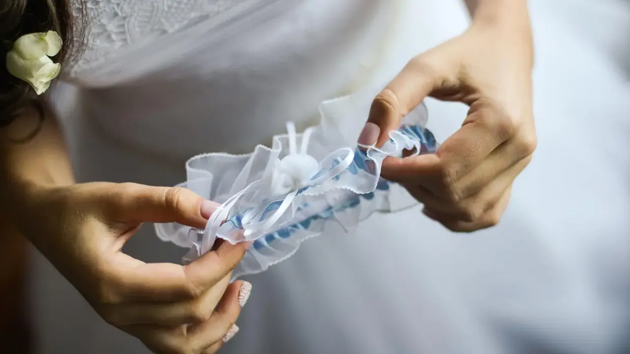 Braut hält ein weißes Strumpfband mit blauen Akzenten. Das Strumpfband ist ein traditionelles Symbol für Glück bei der Hochzeit.