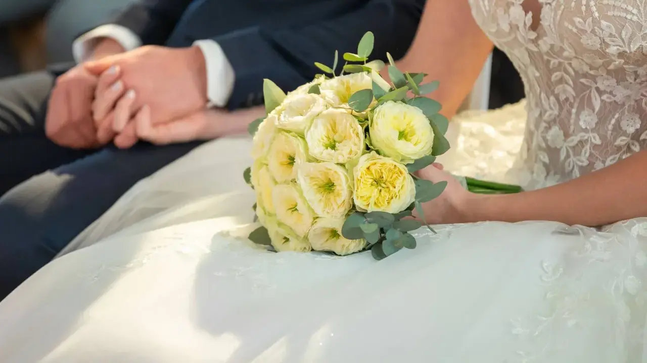 Brautpaar hält Händchen, Brautstrauß mit gelben Rosen. Eine Hochzeit Versicherung gibt Sicherheit für den großen Tag.