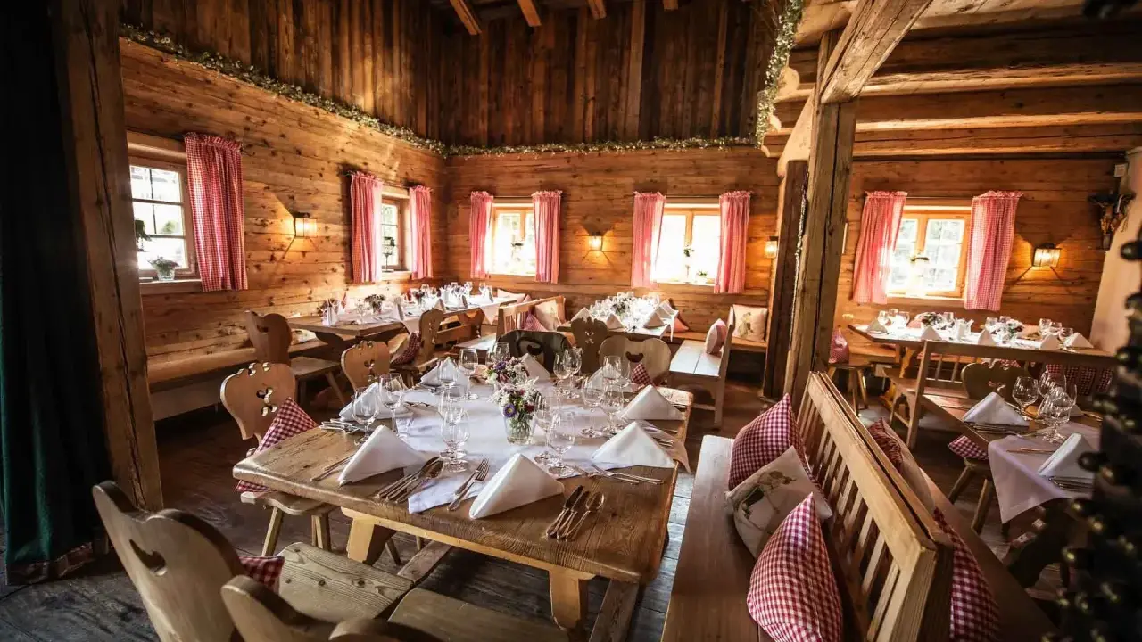 Gemütliche Holzhütte, festlich gedeckte Tische für eine Egerner Alm Hochzeit. Rote Karovorhänge und Blumen schmücken den rustikalen Raum.
