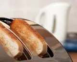 Zwei goldbraune Scheiben Toastbrot ragen aus einem glänzenden Toaster. Ein perfekter Moment, um einen Toast auszusprechen.