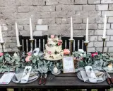 Festlich gedeckter Tisch für eine Hochzeit im Industrial Style mit dreistöckiger Torte, Kerzen und floraler Deko.