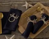 Serviettenringe selber machen: Dunkle Stoffservietten mit rustikalen Geweih-Motiven aus Jute, dazu goldene Besteckteile und Papiersterne.