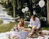 Familie feiert Hochzeit mal anders: Picknick am See mit Ballons und Blumen.
