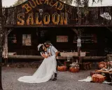 Ein Brautpaar feiert seine western hochzeit vor einem Saloon. Sie tanzen ausgelassen, umgeben von rustikaler Deko.
