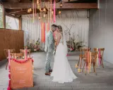 Brautpaar im boho style wedding, umgeben von Blumen und Bändern. Ein Willkommensschild steht im Vordergrund.