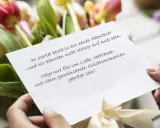 Hände halten eine Karte mit emotionalen Hochzeitswünschen vor einem Tulpenstrauß.