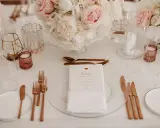 Ein festlich gedeckter Tisch mit Blumen, Gläsern und roségoldenem Besteck. Ein Hochzeitsmenü für Susan, perfekt arrangiert vom wedding planer.