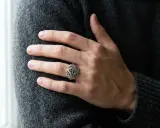 Ein Mann trägt einen detailreichen Ring mit Kreuzmuster an der linken Hand.