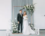 Ein Brautpaar steht vor einem floralen Bogen, bereit, wie heiratet man. Sie strahlen Glück aus.
