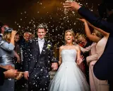 Glückliches Brautpaar bei einer englischen Hochzeit, umgeben von Blütenblättern und jubelnden Gästen.