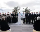 Brautpaar und Hochzeitsgesellschaft vor schneebedeckten Bergen. Eine wunderschöne Hochzeit in den Bergen mit Brautjungfern in schwarzen Kleidern und Männern in Anzügen.