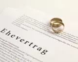 Zwei goldene Eheringe liegen auf einem Dokument mit der Überschrift "Ehevertrag". Eine Ehevertrag Vorlage, die die rechtlichen Vereinbarungen für die Ehe festhält.