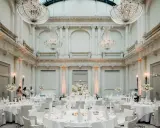 Elegante Tische mit weißen Hussen und Blumenarrangements in einem prunkvollen Saal mit Kronleuchtern – eine besondere Hochzeitslocation.