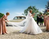 Brautjungfern helfen der Braut mit ihrem Schleier vor einer Hochzeitslimousine.