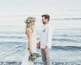 Ein glückliches Paar feiert seine Hochzeit am Strand zu zweit. Die Braut trägt einen Blumenkranz, der Bräutigam ein weißes Hemd.