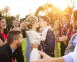 Glückliches Brautpaar küsst sich im Konfettiregen, umgeben von lachenden Gästen. Tolle Spiele zur Hochzeit!