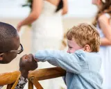 Ein Mann mit Brille hält die Hand eines Jungen. Im Hintergrund heiratet mein Sohn.