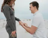 Ein Mann kniet am Strand und steckt seiner lachenden Partnerin einen Ring an den Finger. Ein Moment, der die tiefe **Verlobung Bedeutung** symbolisiert.