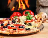 Eine dampfende Pizza mit Salami, Oliven und Paprika, perfekt für den Mitternachtssnack zur Hochzeit, vor einem knisternden Kaminfeuer.
