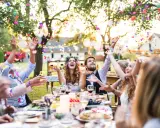 Glückliche Gäste werfen Konfetti bei einer fröhlichen Garten Hochzeit. Das Brautpaar lacht ausgelassen.