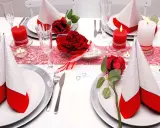 Festlich gedeckter Tisch für eine rot-weiße Hochzeit. Rote Rosen und Kerzen sorgen für romantische Stimmung.